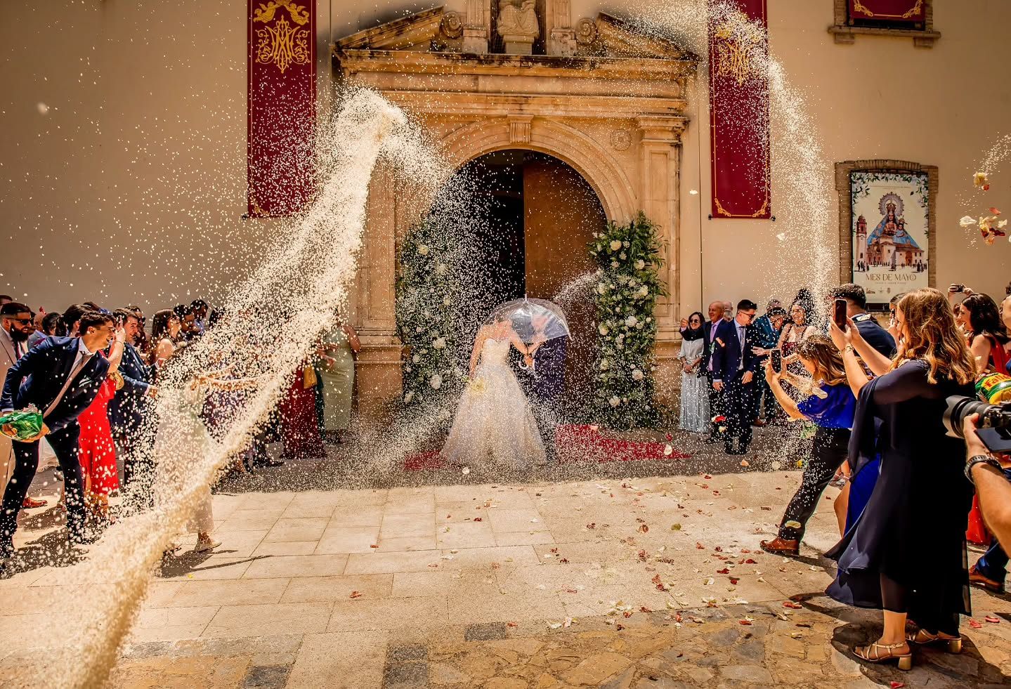 Los novios se besan bajo dos arcos de arroz lanzado a la salida de la iglesia, rodeados de invitados